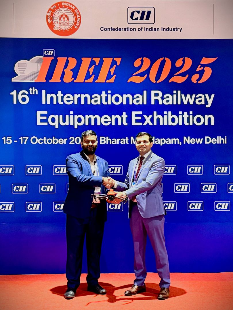 Two men holding a drone shake hands infront of a banner sating IREE 2025 - 16th international railway equipment exhibition