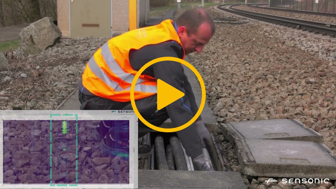 A video thumbnail with a play icon in the centre. The image is of a man reaching into a railway cable duct. Inset is a graph showing any movement of cables being detected. 