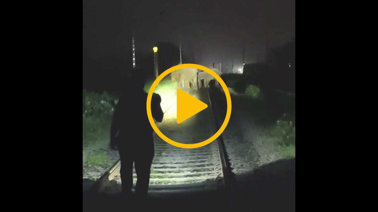 A video thumbnail with a play icon in the centre - The video shows a railway at night. Torch light reveals a family of elephants standing on the railway track